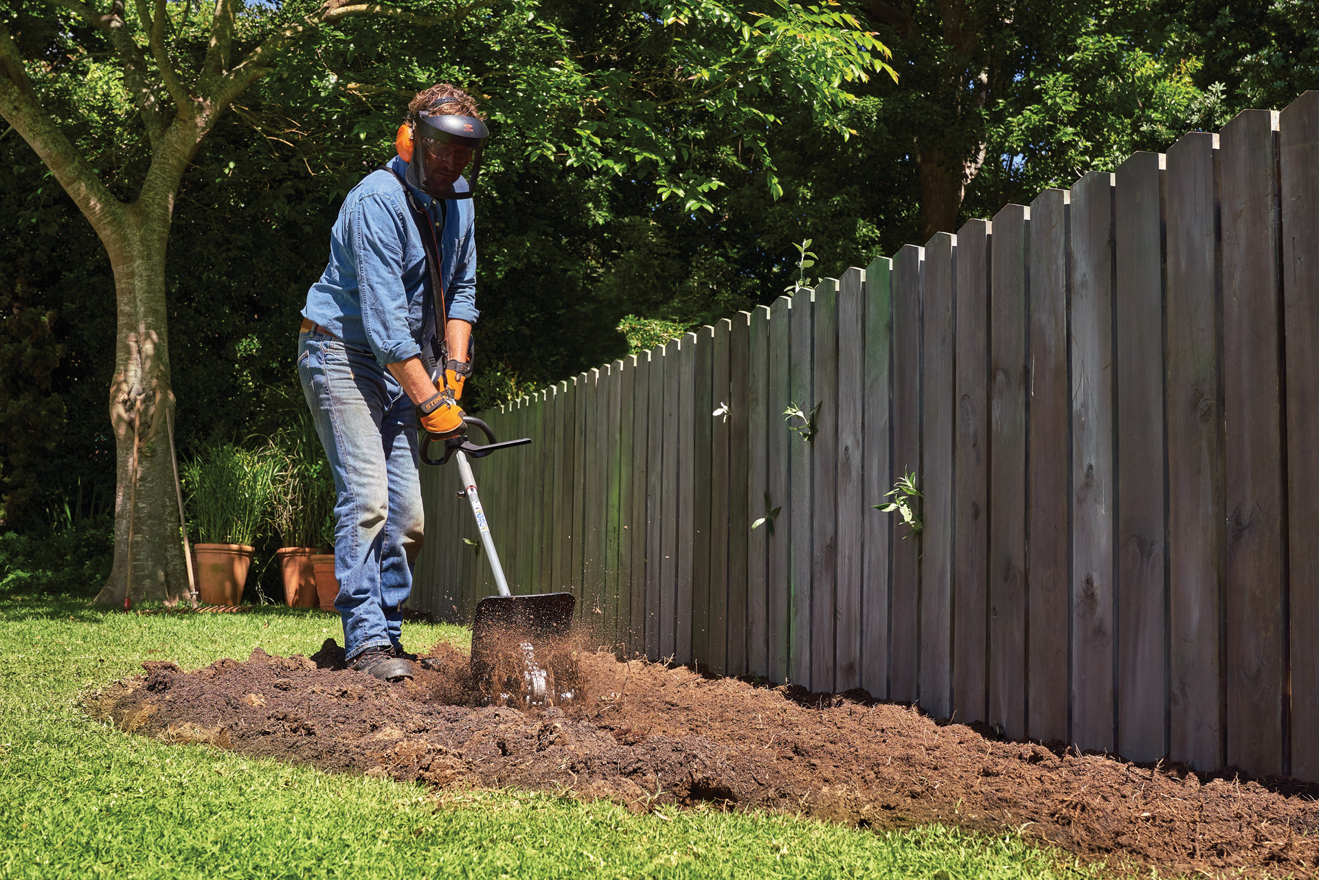 Personne avec un équipement de protection cultive la terre dans un jardin avec un combisystème STIHL avec sarcleuse