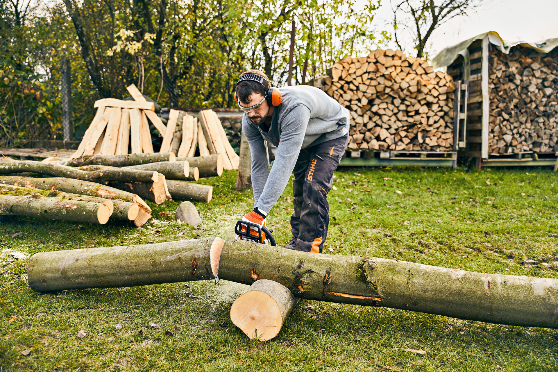 Uomo con occhiali di protezione e protezioni acustiche taglia un tronco di legno con una motosega a benzina STIHL MS 180